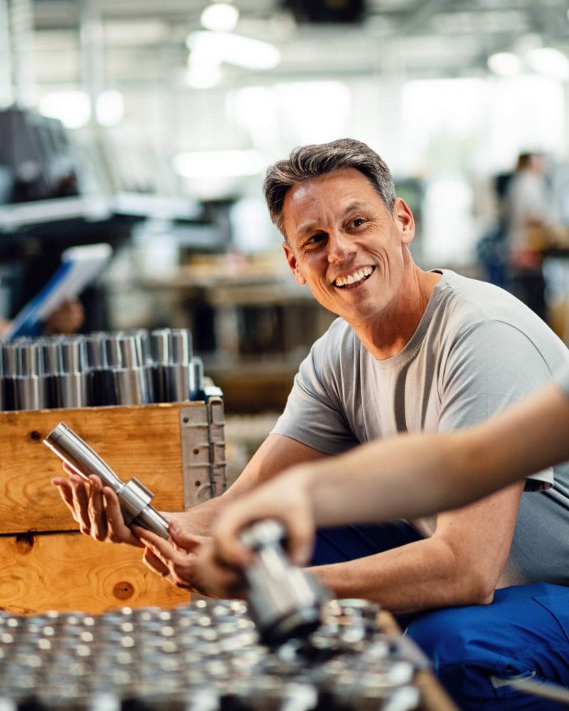 Two happy steel workers preparing manufacture products for the distribution and communicating in industrial facility. Focus is on mid adult worker.